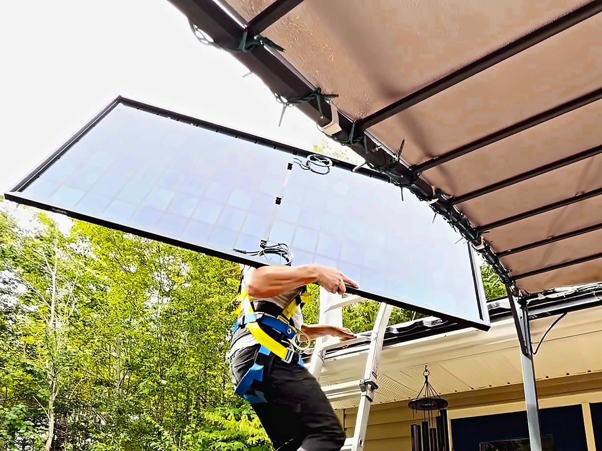 An installer carrying a solar panel up a ladder to a Nova Scotia rooftop