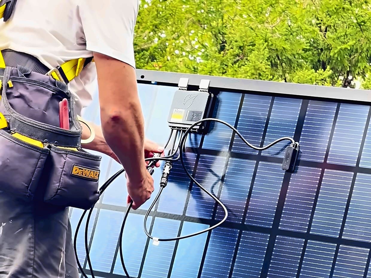 An installer in a safety harness connecting the cables on a rooftop solar panel