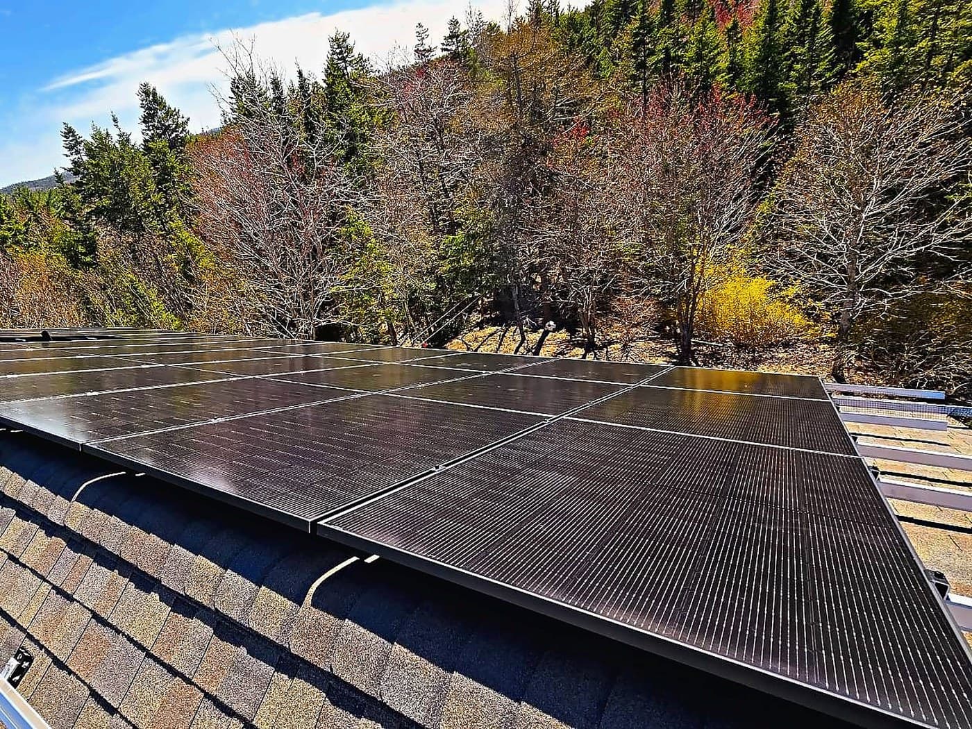 An all-black solar array installed across a shingle roof, with a wooded Nova Scotia hillside behind it