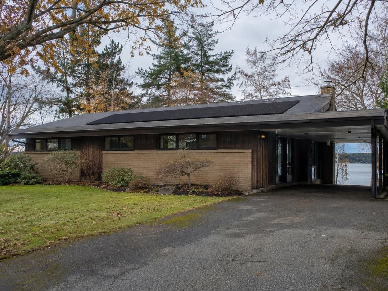 A mid-century brick and wood ranch home on a lake with a rooftop solar array and carport
