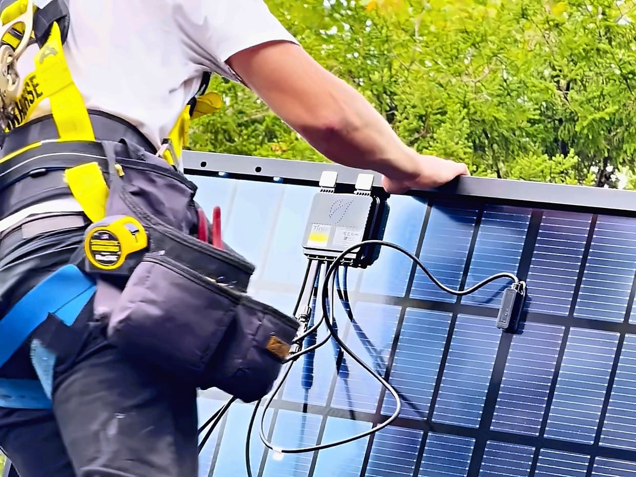 An installer landing a solar panel on a rooftop, its junction box and connector leads in view